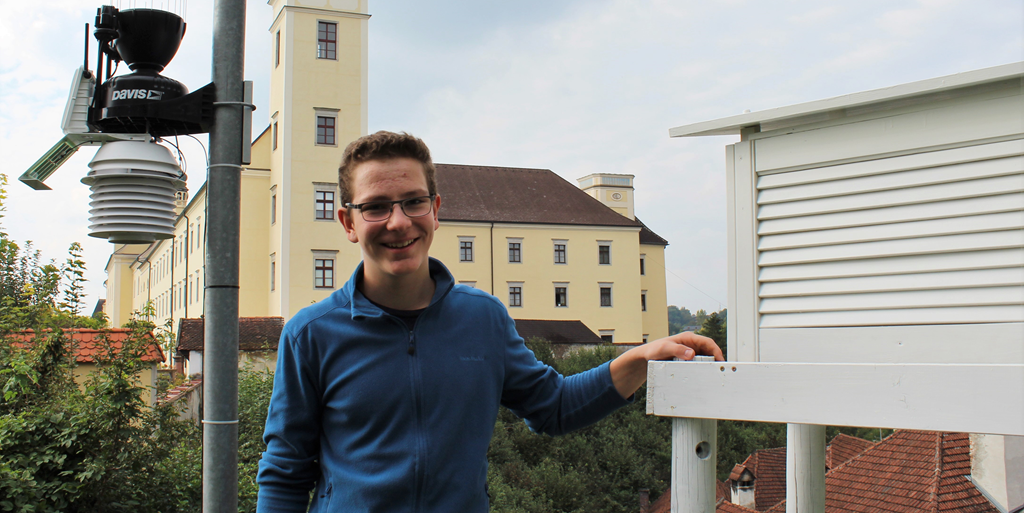 Paul Stöttinger neben einer weißen Wetterhütte zu Temperaturmessung, im Hintergrund das Stift Lambach